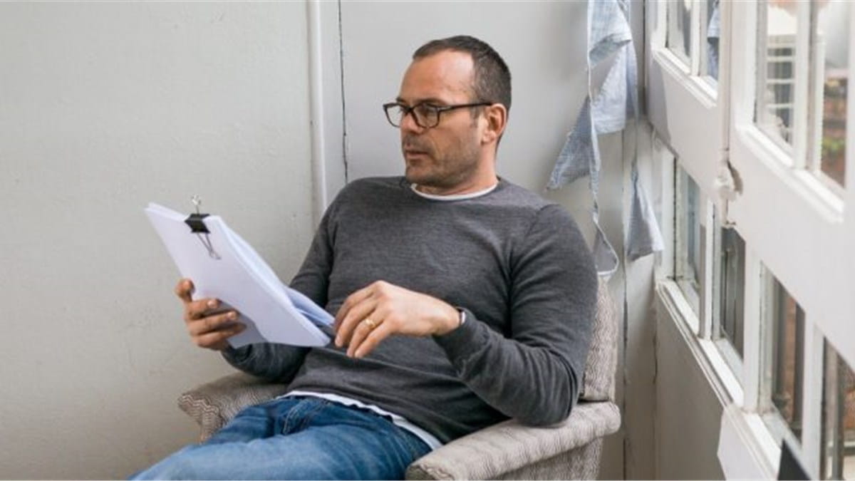 Ein Mann sitzt in einem Stuhl und liest Unterlagen.